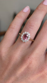 Antique-inspired rose-pink tourmaline and diamond cluster engagement ring featuring an oval rose-pink tourmaline surrounded by brilliant-cut diamonds, displayed on a hand.