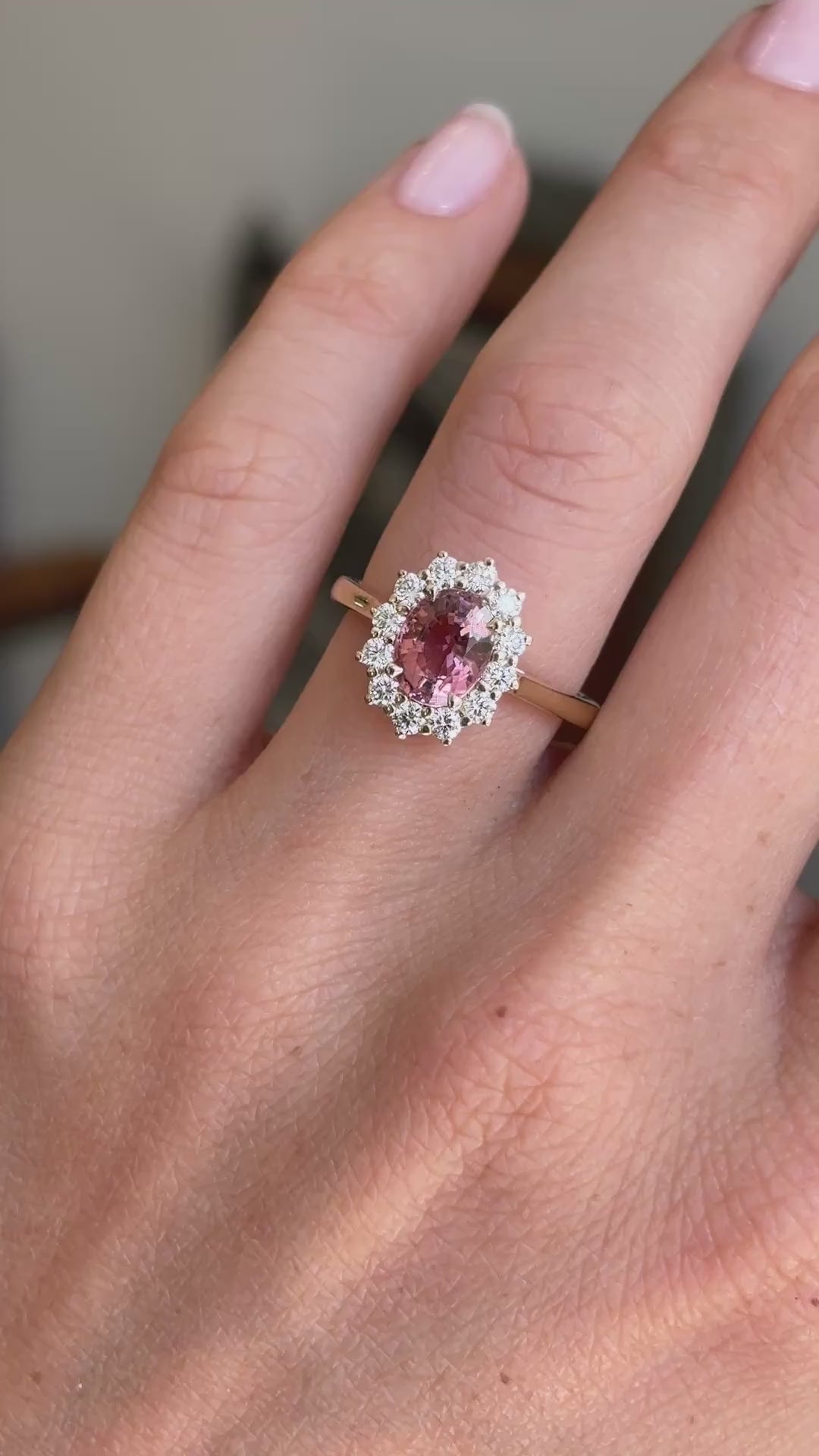 Antique-inspired rose-pink tourmaline and diamond cluster engagement ring featuring an oval rose-pink tourmaline surrounded by brilliant-cut diamonds, displayed on a hand.