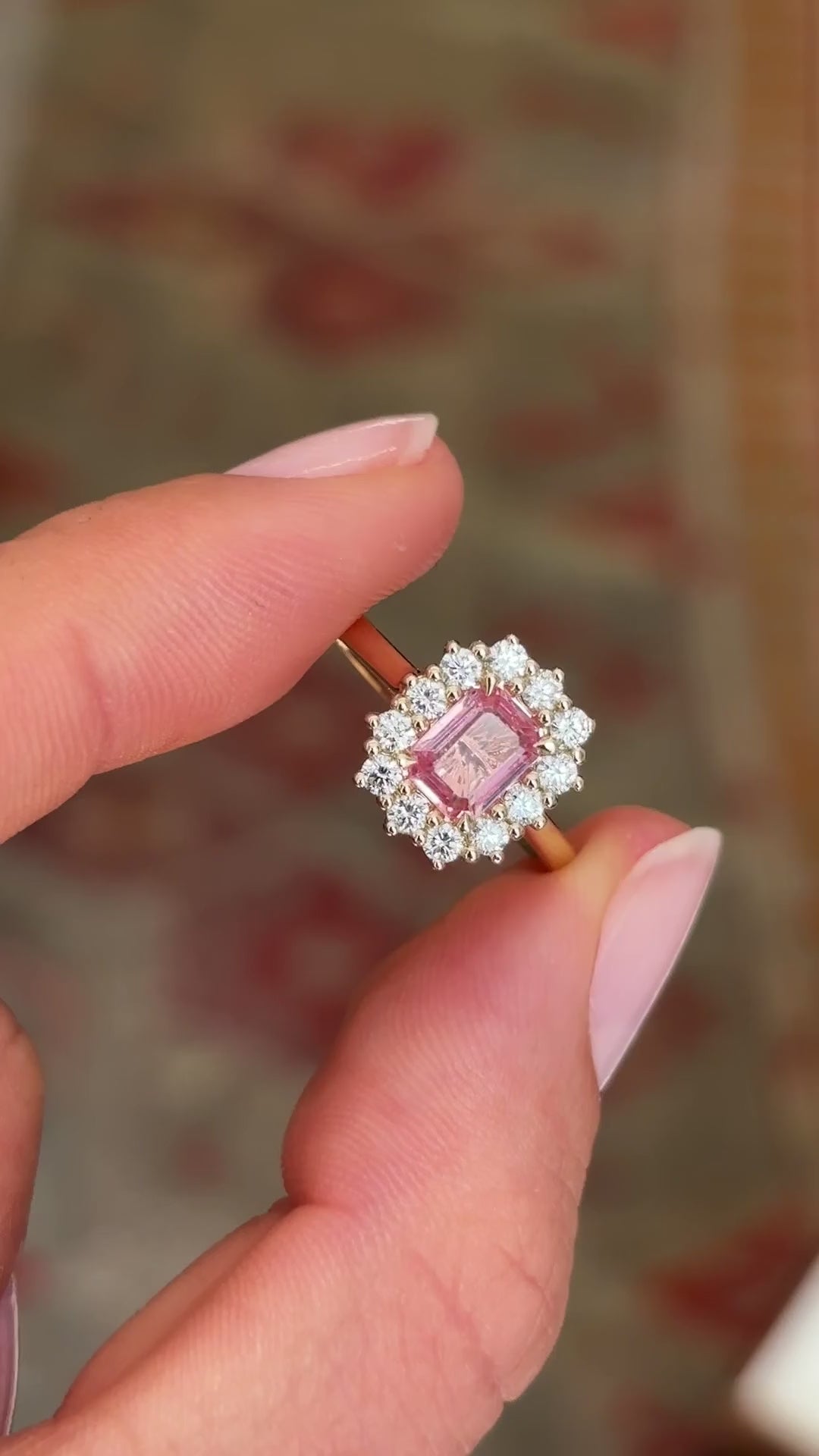 Antique-inspired sunset pink sapphire and diamond cluster engagement ring with an octagon-cut sunset pink sapphire centre stone and sparkling diamond halo, displayed on a hand.