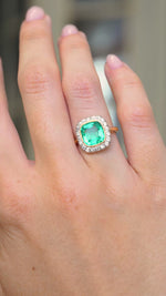 A video of an antique Belle Époque era yellow gold engagement ring featuring an emerald and diamonds worn on the hand held at a distance to show the proportions and slowly turned. 