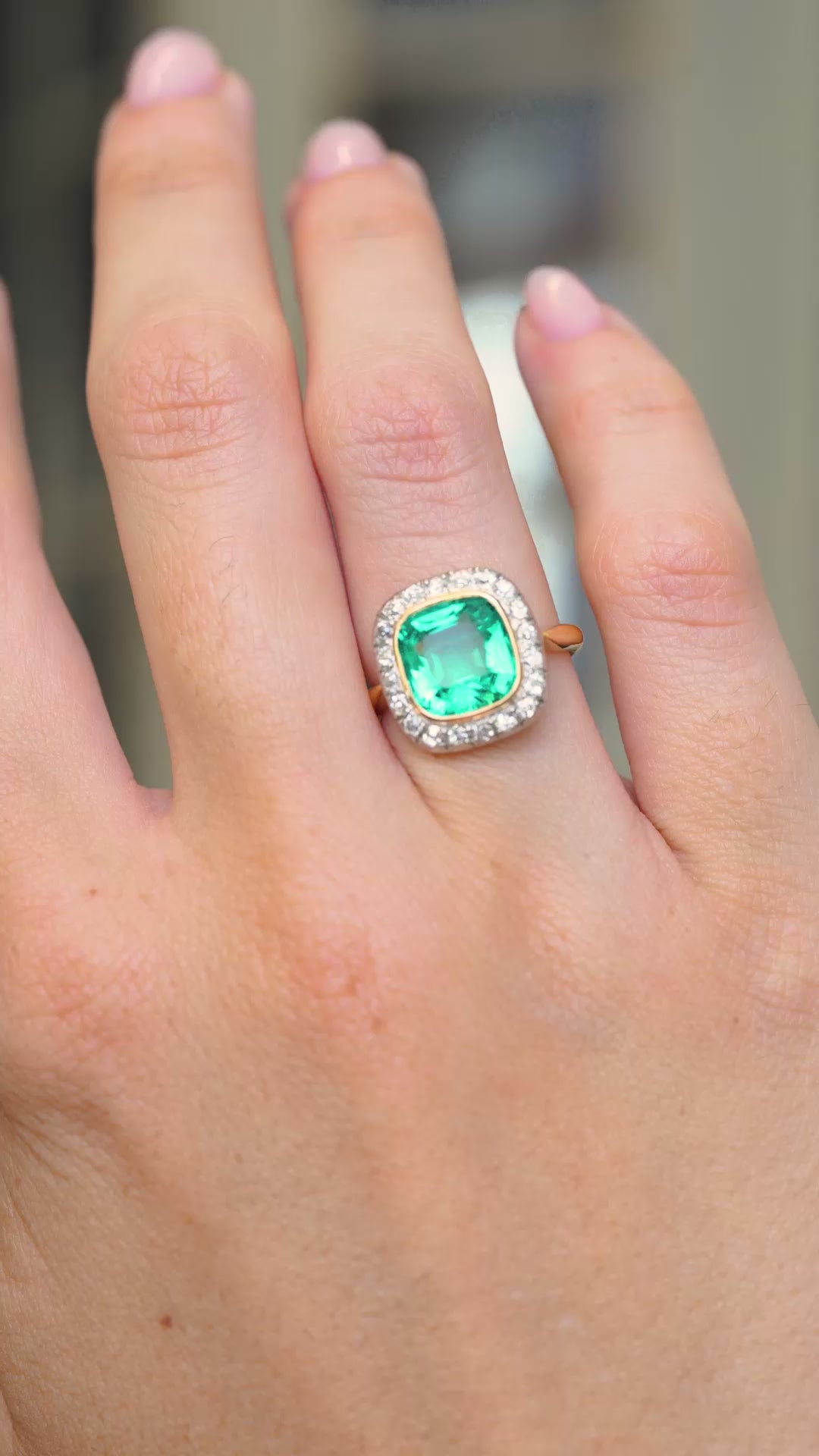 A video of an antique Belle Époque era yellow gold engagement ring featuring an emerald and diamonds worn on the hand held at a distance to show the proportions and slowly turned. 
