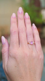 Pink oval sapphire and diamond three-stone engagement ring worn on hand with subtle motion.