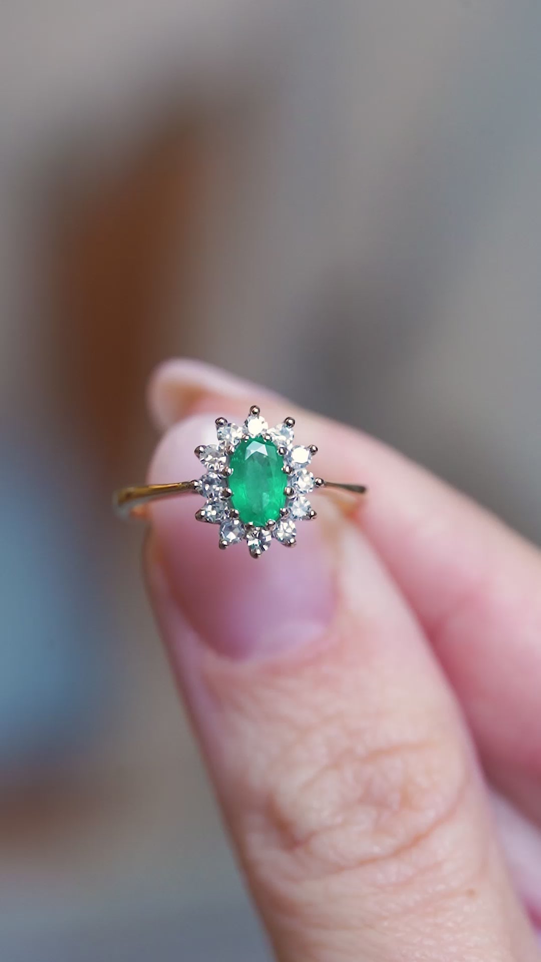 Close detail video of vintage 1980s emerald and diamond cluster ring with raised diamond setting between fingers.