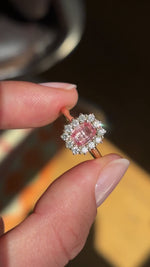 Antique-inspired sunset pink sapphire and diamond cluster engagement ring featuring an octagon-cut sunset pink sapphire encircled by brilliant-cut diamonds, held by hand for detailed viewing.