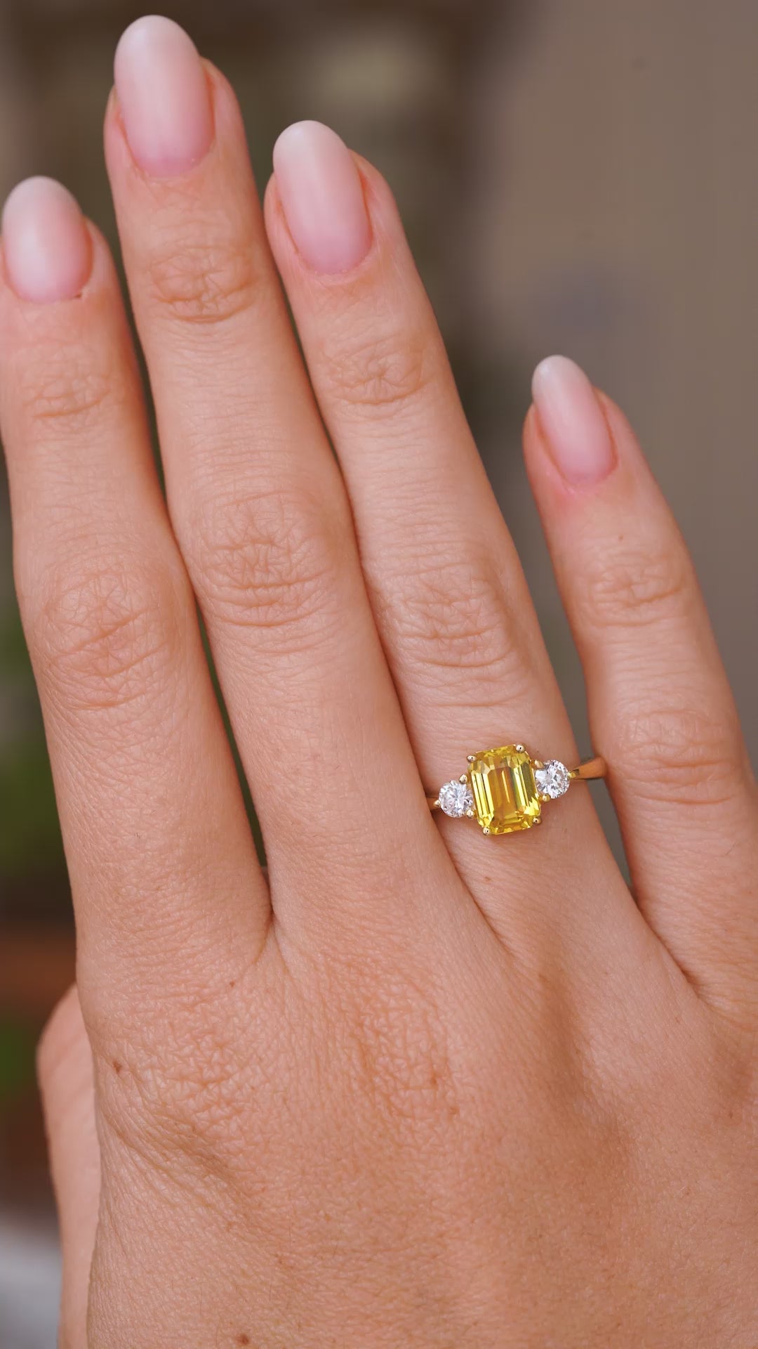 A video of a hand wearing an Antique-inspired, Yellow sapphire and diamond three-stone engagement ring, yellow gold and the hand slowly turns