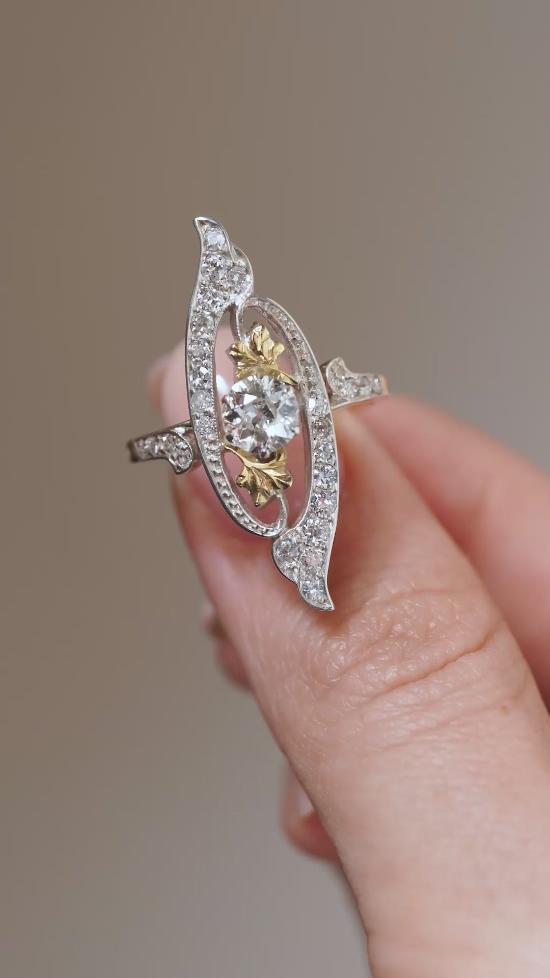 Video: Art Nouveau diamond cross-over ring held between fingers, showing its intricate diamond-set curves and central old-cut diamond.