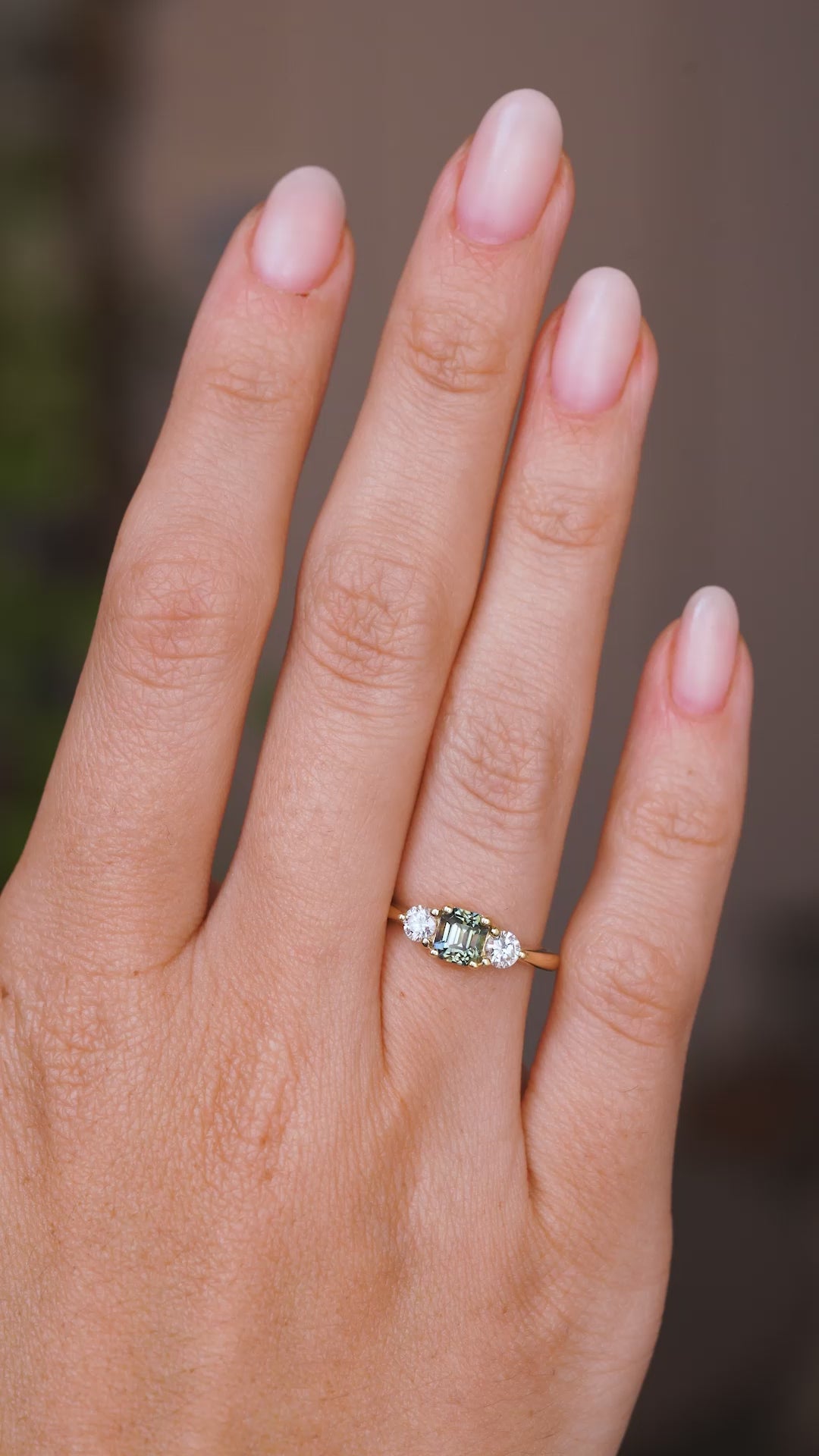 A video of a hand wearing an Antique-inspired, Teal sapphire and diamond three-stone engagement ring in yellow gold.