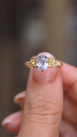 A close up video of a Vintage-inspired, Blue sapphire and diamond engagement ring in yellow gold held between two fingers and rotated slowly to display the profiles of the ring. 