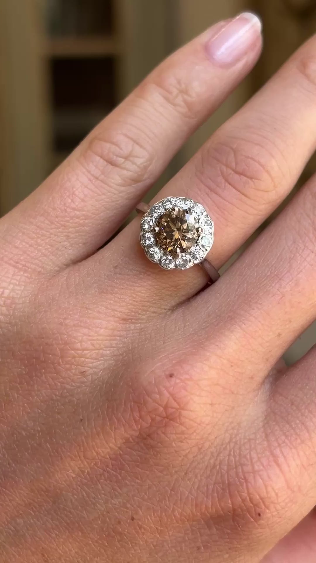 Vintage 1950s cinnamon brown diamond cluster engagement ring featuring a cinnamon brown diamond surrounded by a halo of diamonds, displayed on a hand.
