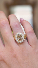 A close up video of a vintage brown diamond cocktail ring with a diamond halo worn on the hand.