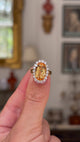 Imperial topaz and diamond cluster ring with gold band held and rotated to give perspective.