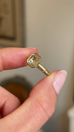 Close up video of two fingers rotating an Antique-inspired Pale yellow sapphire solitaire engagement ring in gold against a blurred indoor setting.