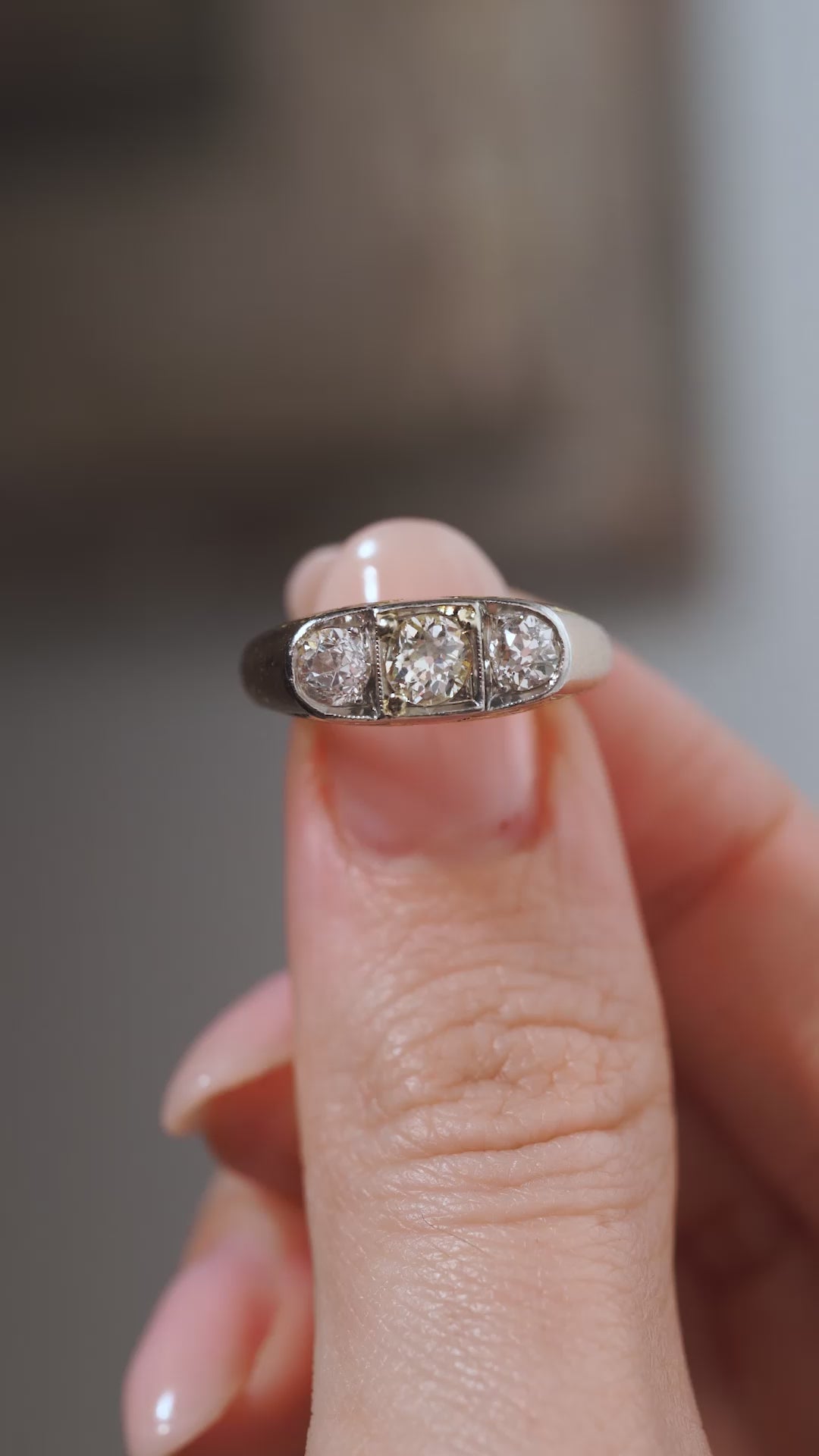 A close-up video of an antique Edwardian diamond three-stone ring held between fingers, showcasing the three old-cut diamonds and distinctive platinum and yellow gold setting.