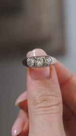 A close-up video of an antique Edwardian diamond three-stone ring held between fingers, showcasing the three old-cut diamonds and distinctive platinum and yellow gold setting.