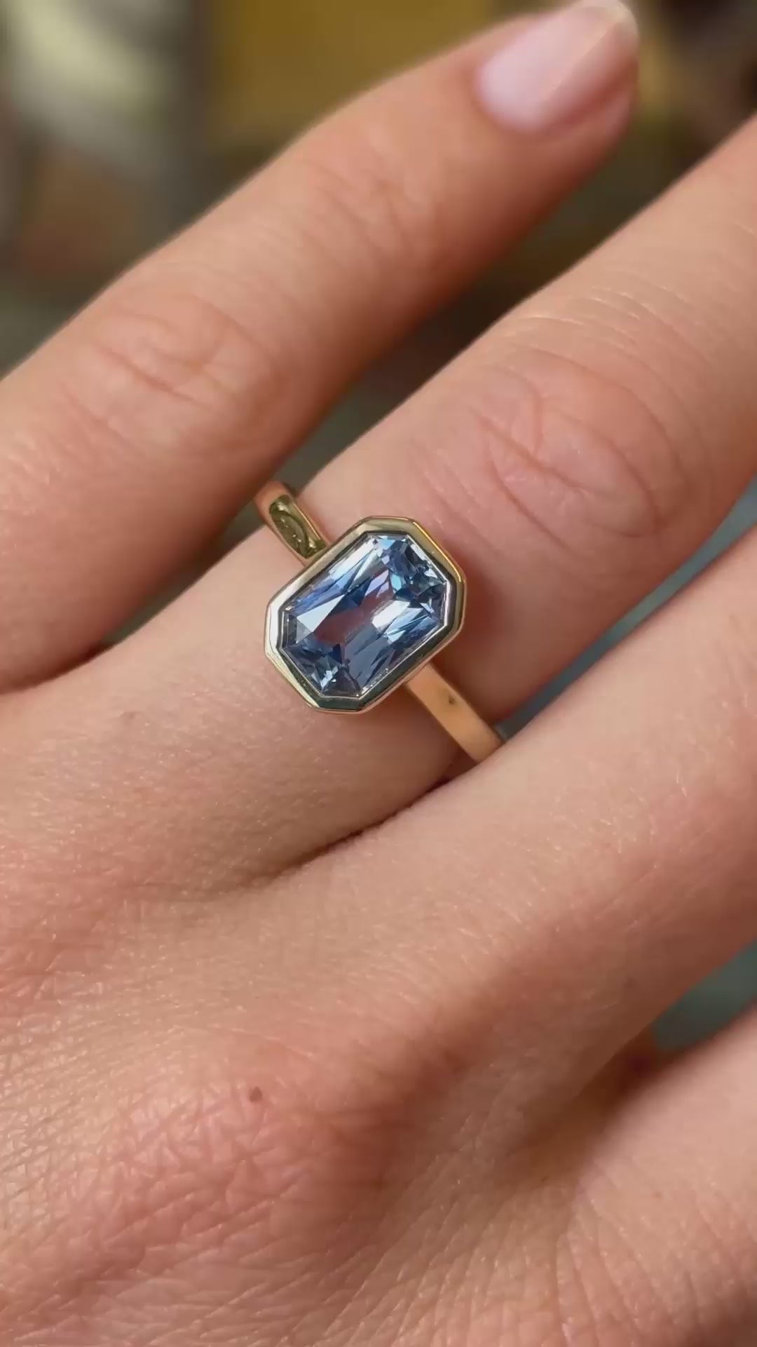 A close up of an Antique-inspired pale blue sapphire solitaire engagement ring in yellow gold shown in video on a finger.
