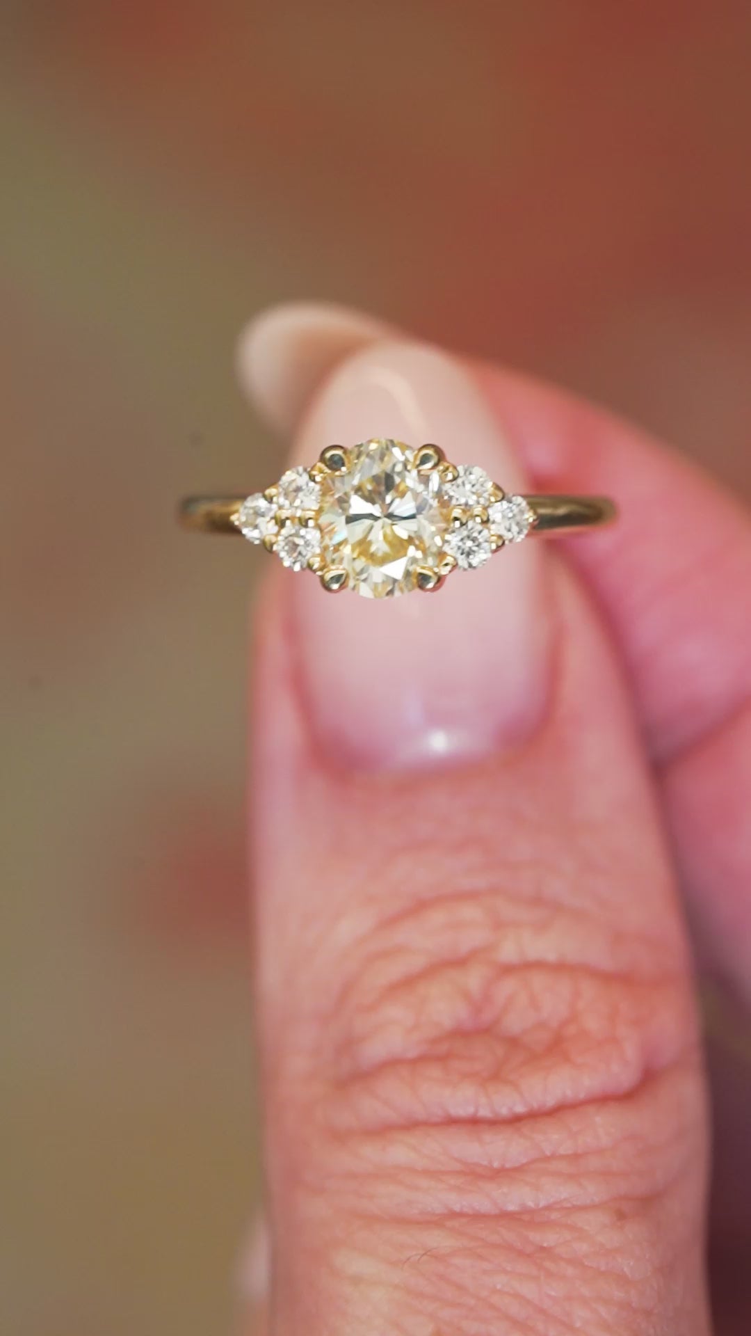 Antique-inspired primrose yellow diamond cluster tre-foil engagement ring held between fingers showing ring details.