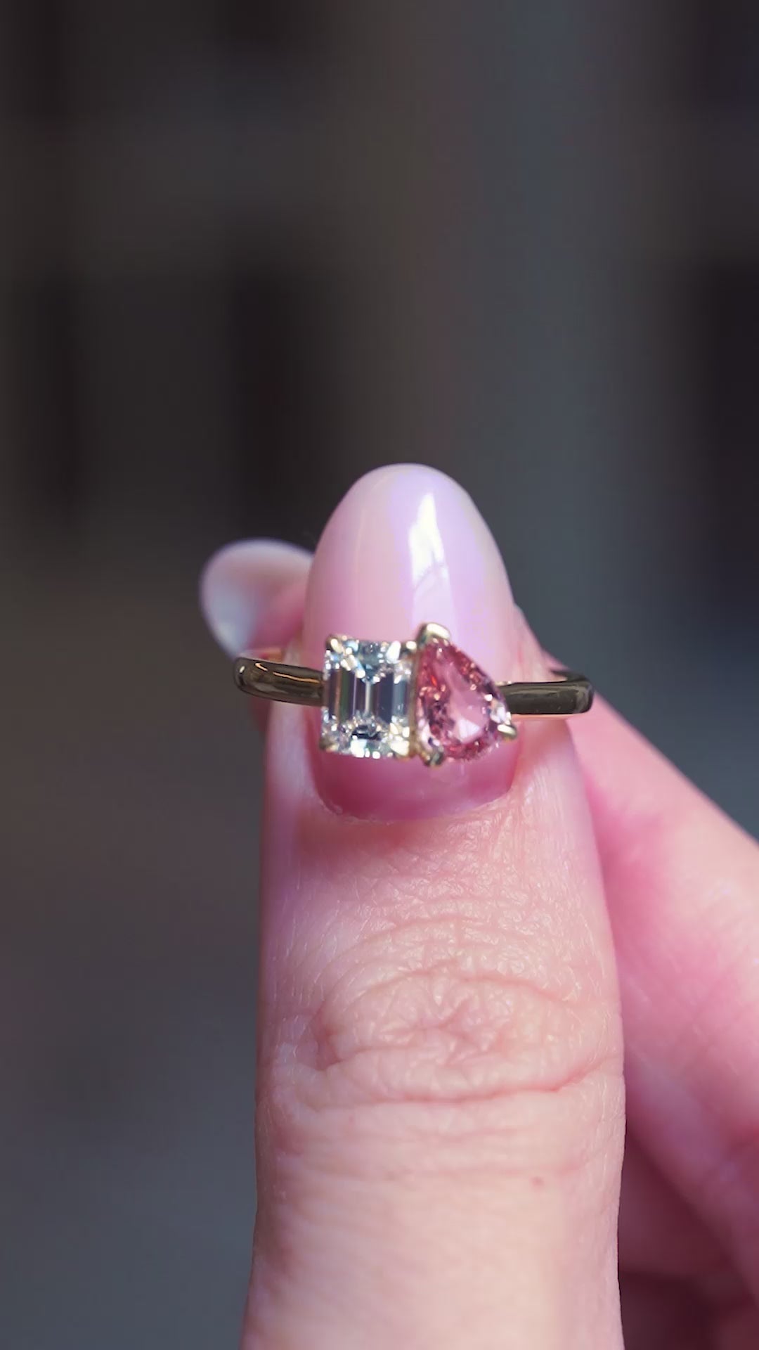 Peach coloured sapphire and diamond Toi et Moi engagement ring held between fingers showing ring details.