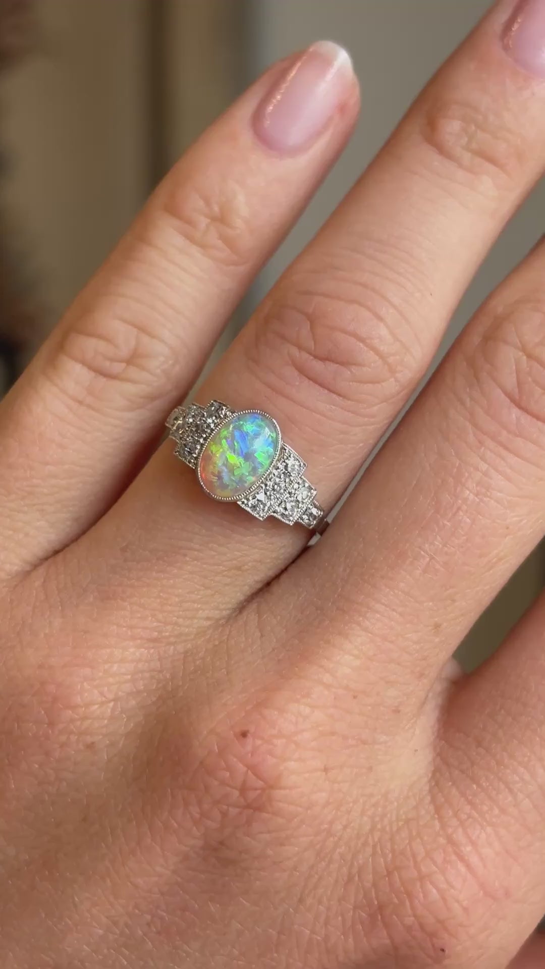 Video of an antique Art Deco opal and diamond cluster ring worn on hand, showcasing the opal's colourful play-of-light and sparkling diamonds that frame it on either side. 