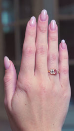 Peach coloured sapphire and diamond Toi et Moi engagement ring worn on hand showing subtle motion.