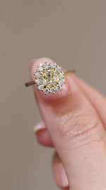 A close-up video of the yellow diamond engagement ring held between fingers, showcasing the central diamond's facets and intricate cluster setting.