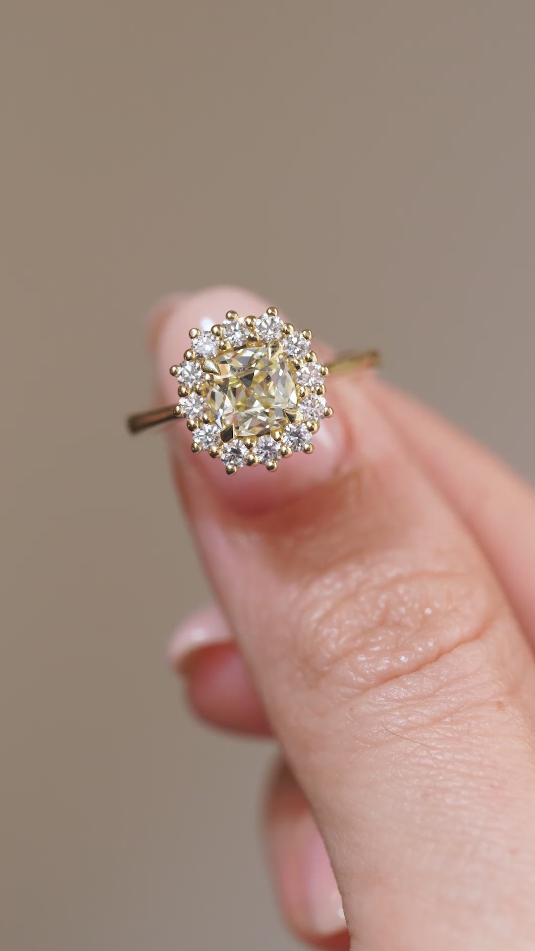 A close-up video of the yellow diamond engagement ring held between fingers, showcasing the central diamond's facets and intricate cluster setting.