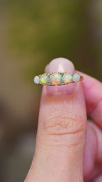 A close-up of an antique opal and diamond half-hoop ring in yellow gold shown in video between fingers. 