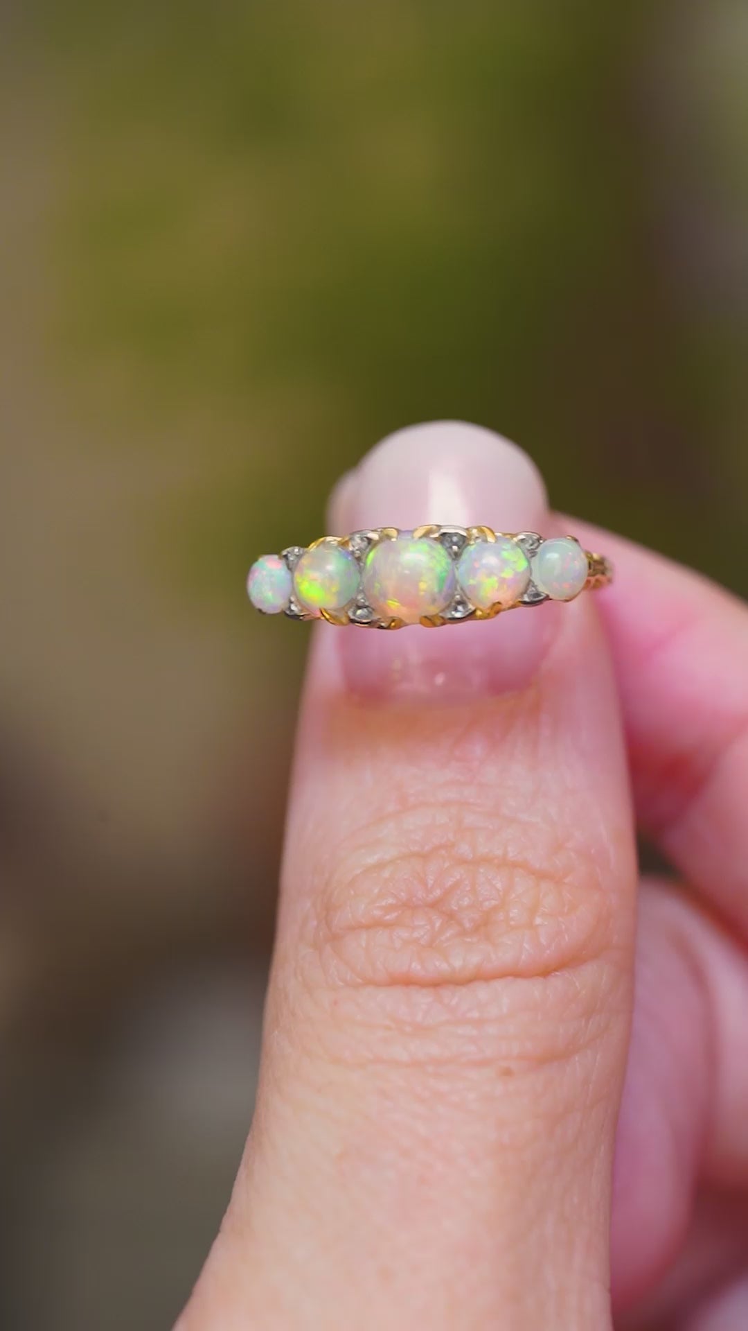 A close-up of an antique opal and diamond half-hoop ring in yellow gold shown in video between fingers. 
