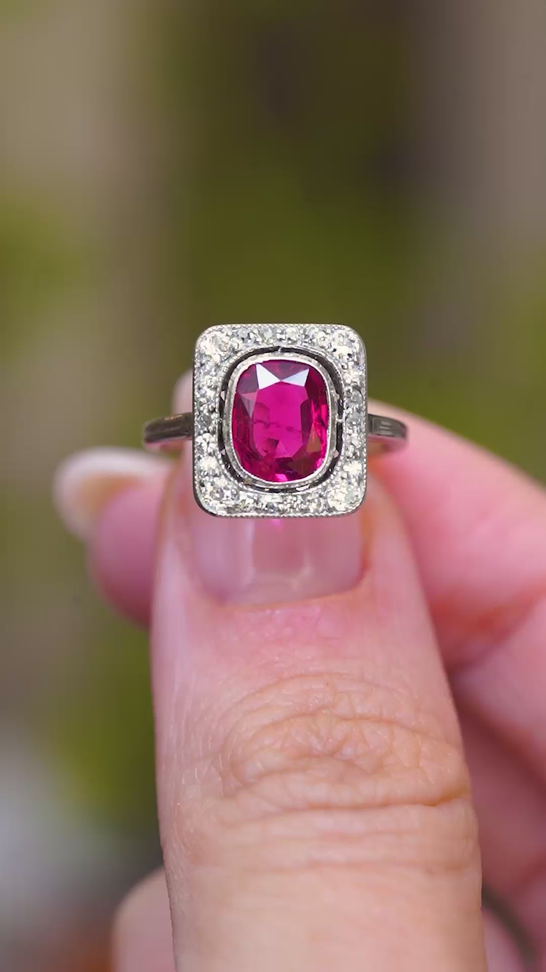 A video of an antique red spinel and diamond cluster ring held between the fingers showcasing the ring details.