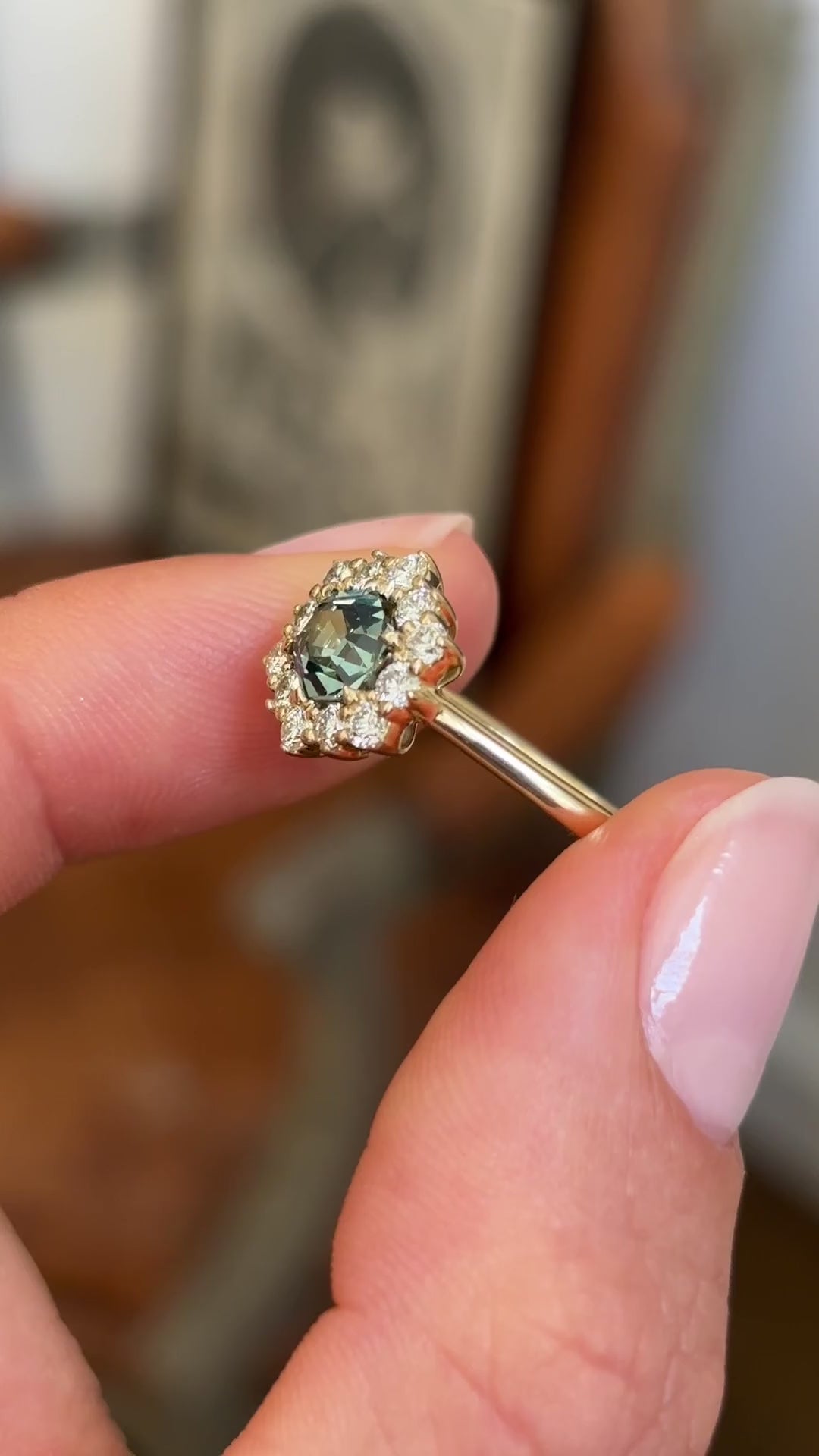 Teal hexagon-cut sapphire and diamond cluster engagement ring with a hexagon-cut teal sapphire centre stone and sparkling diamond halo, held by hand for detailed viewing.