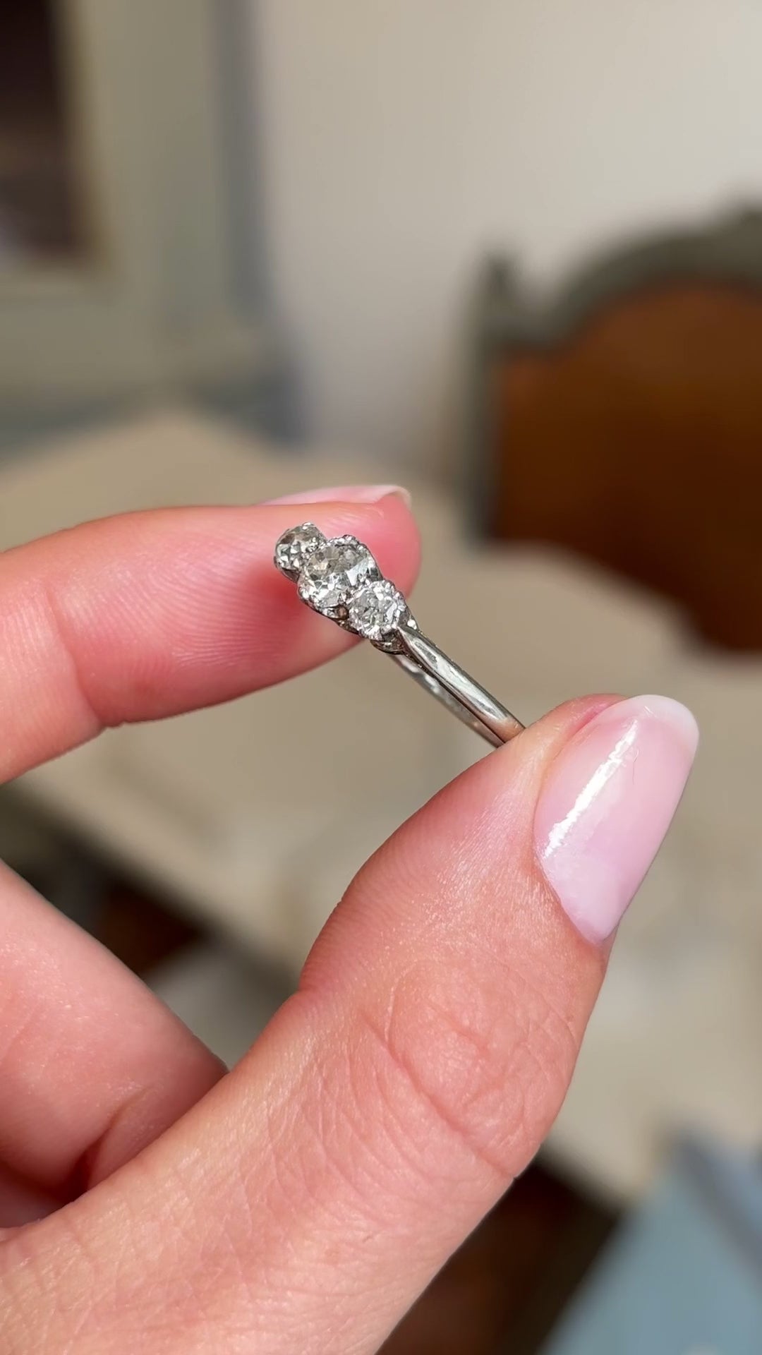 Close up video of a white gold Vintage 1940s diamond three-stone engagement ring rotated between two fingers slowly to display the three old-mine cut diamonds