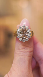 Vintage brown diamond cocktail ring with an oval fancy coloured brown diamond framed by a halo of brilliant-cut diamonds being held between fingers showing ring details.