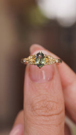 A video of a Vintage-inspired, Green sapphire and diamond engagement ring held in between the fingers