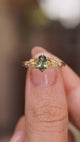 A video of a Vintage-inspired, Green sapphire and diamond engagement ring held in between the fingers