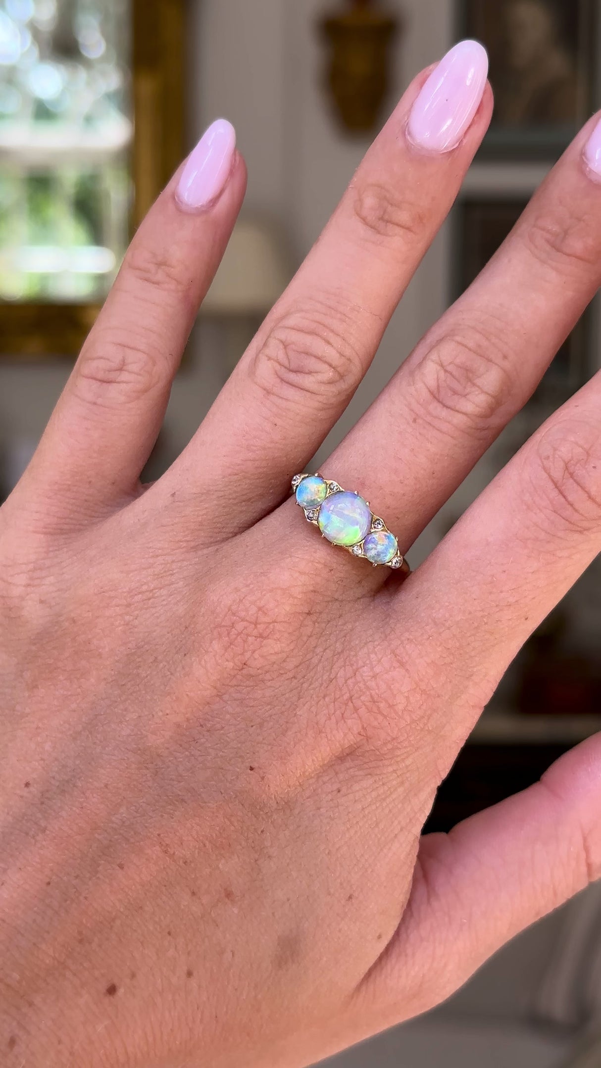 Opal and diamond three stone ring, worn on hand and moved away from lens to give perspective,front view. 