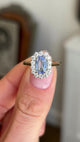 Video of an Antique-inspired, blue sapphire and diamond cluster engagement ring in gold, held between two fingers and rotated to see the side profiles.