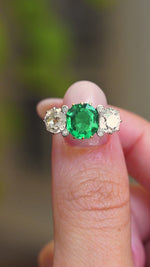 A close-up video of an antique Edwardian octagon-cut emerald and old-mine diamond three-stone engagement ring held between fingers, showing the various ring details. 