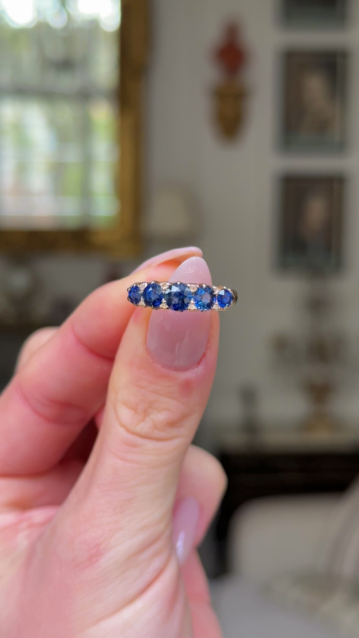 sapphire and diamond five stone ring held in fingers and rotated to give perspective.