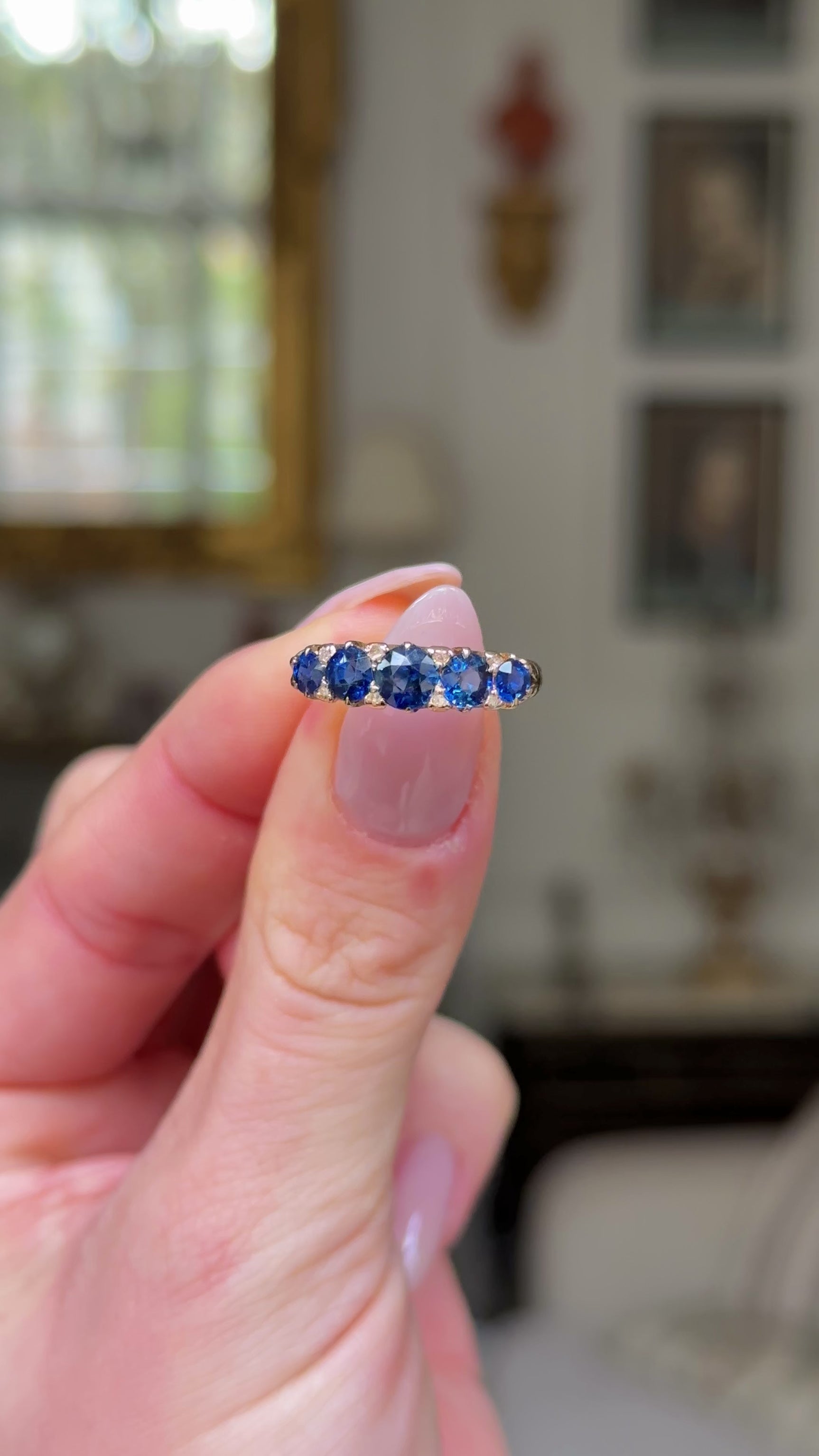 sapphire and diamond five stone ring held in fingers and rotated to give perspective.