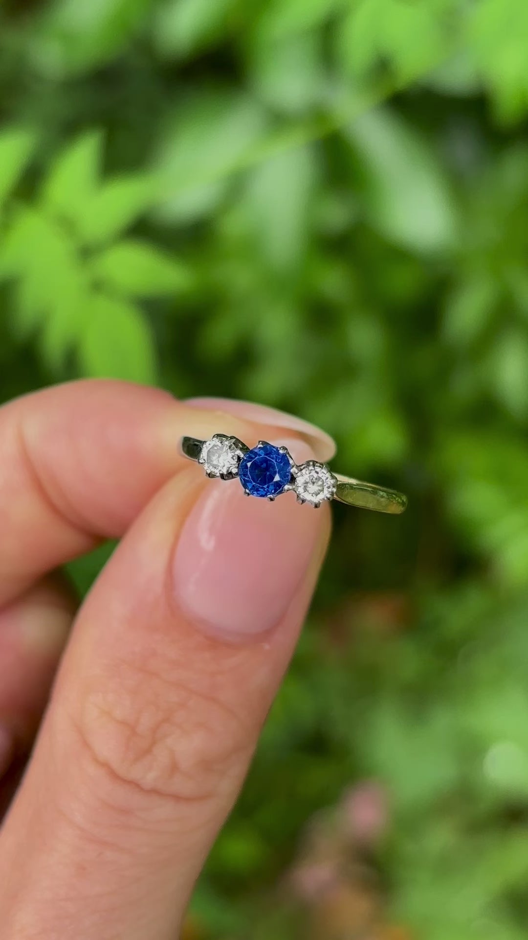 Antique, Edwardian sapphire and diamond three-stone ring held in fingers.