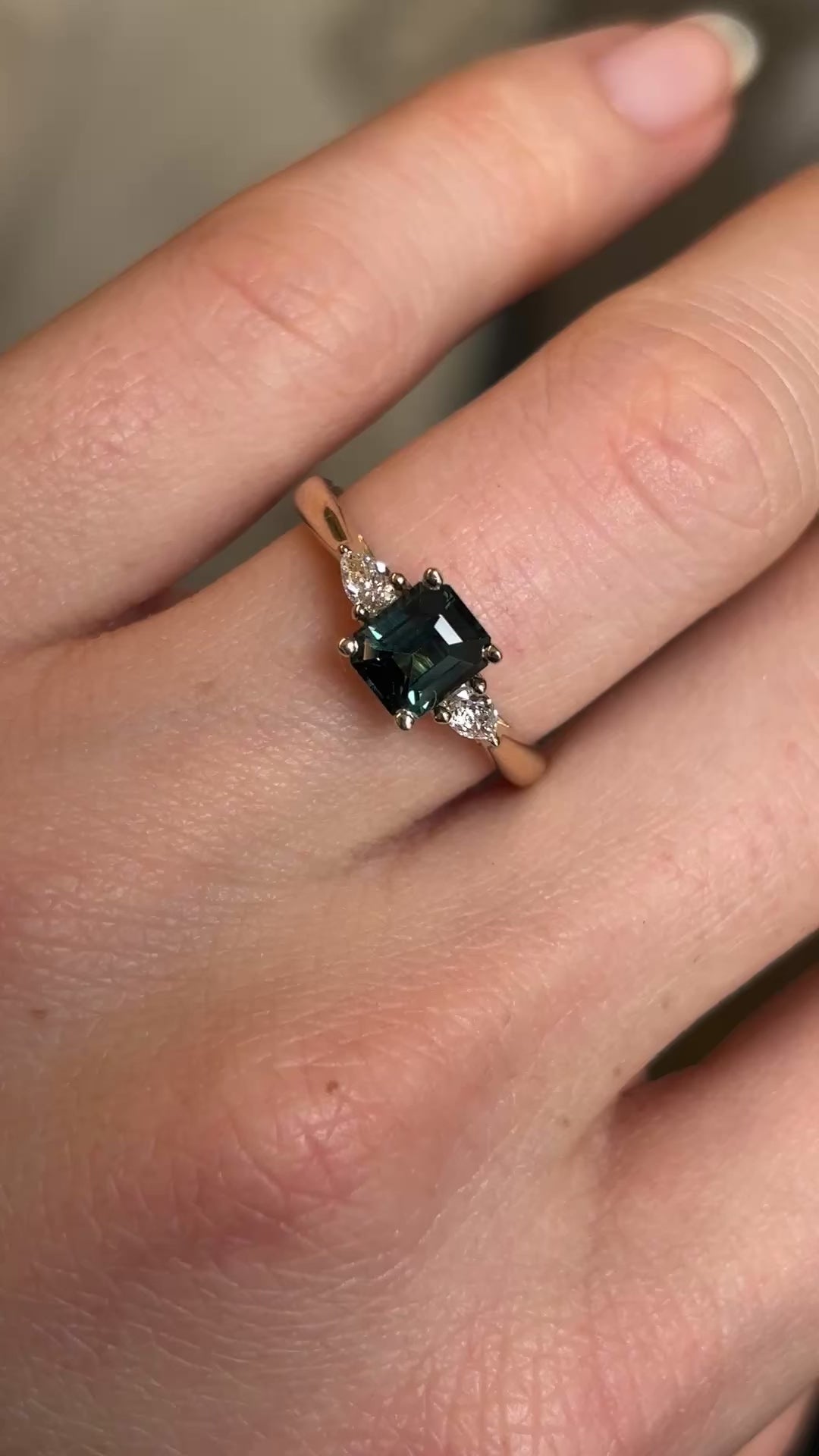 Green sapphire and diamond three-stone engagement ring on hand from a distance to show scale