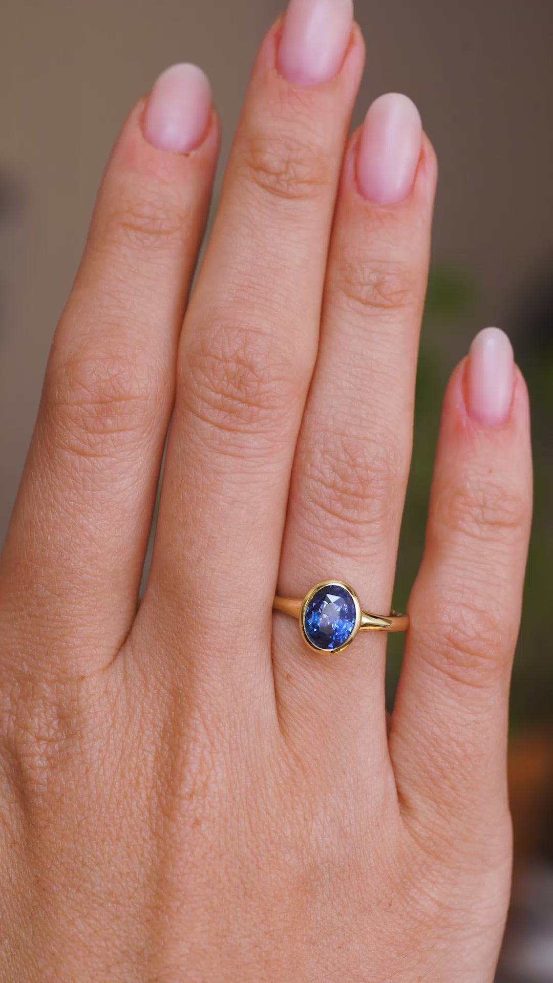 A video of a solitaire engagement ring worn on a wedding finger.  Rotated slowly to display the antique-inspired yellow gold bezel setting of the Sri Lankan blue sapphire and the profile of the setting and band once worn. 