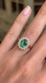 Close-up video of an antique-inspired yellow gold cluster ring showcasing an oval-cut emerald framed by sparkling diamonds, highlighting rich green colour, brilliance and fine craftsmanship.