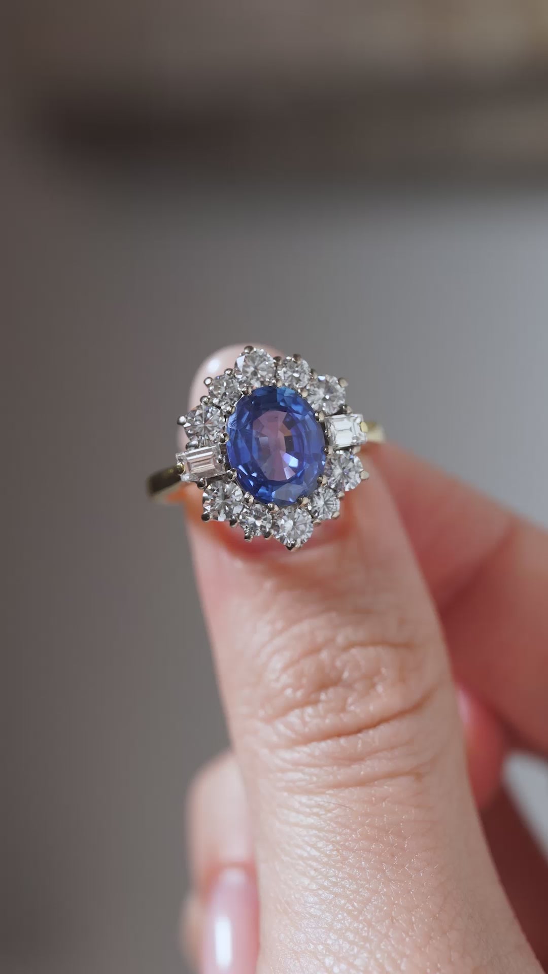 A close-up video of a vintage 1980s blue sapphire and diamond cluster ring held between fingers, showcasing the rich blue sapphire and surrounding diamond arrangement.