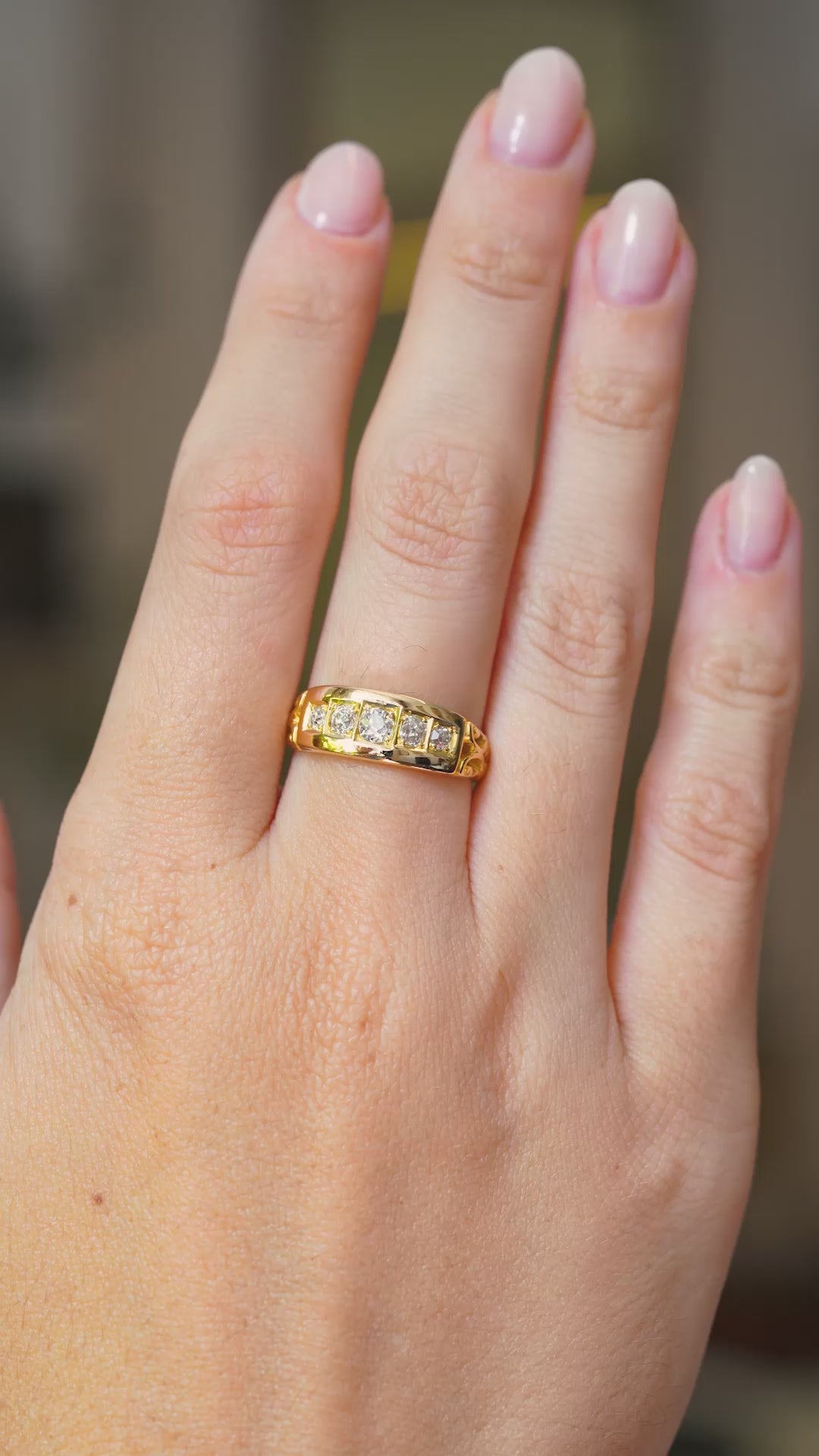 An Antique, Victorian diamond five-stone engagement ring gypsy style and mounted in yellow gold worn on the hand and shown at a distance in a video of the hand moving.