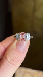 Lab-pink diamond & white diamond three-stone ring in dazzling natural light showing showing the pink colours of the central diamond.