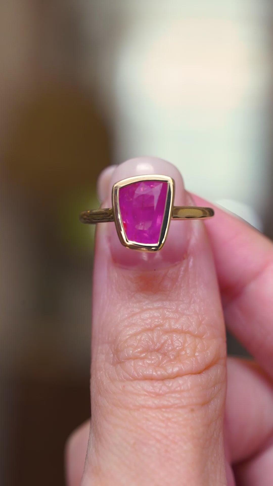 A vintage-inspired, pink ruby solitaire engagement ring in yellow gold, showing the ring details in video held between fingers.