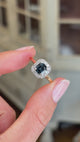 Antique Art Deco sapphire and diamond cluster engagement ring featuring a blue sapphire centre stone surrounded by a geometric diamond cluster, held by hand for detailed viewing.