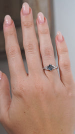 A video of the vintage-inspired sapphire engagement ring worn on a hand, displaying its subtle blue-grey tones and delicate laurel leaf-inspired shoulders.