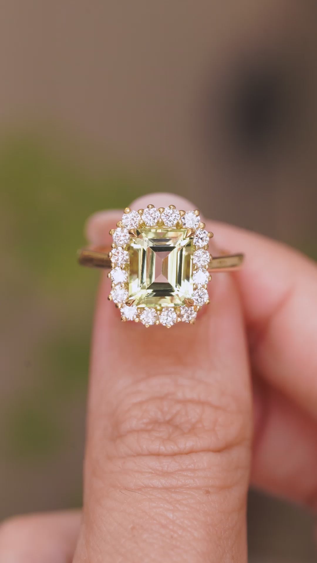 A close-up video of an Antique-inspired, Green beryl and diamond cluster engagement ring in yellow gold.  Held between two fingers and rotated slowly to show the basket setting and yellow gold band. 