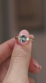 A close-up video of the sapphire engagement ring held between fingers, showcasing the gemstone's colour and diamond shoulders.